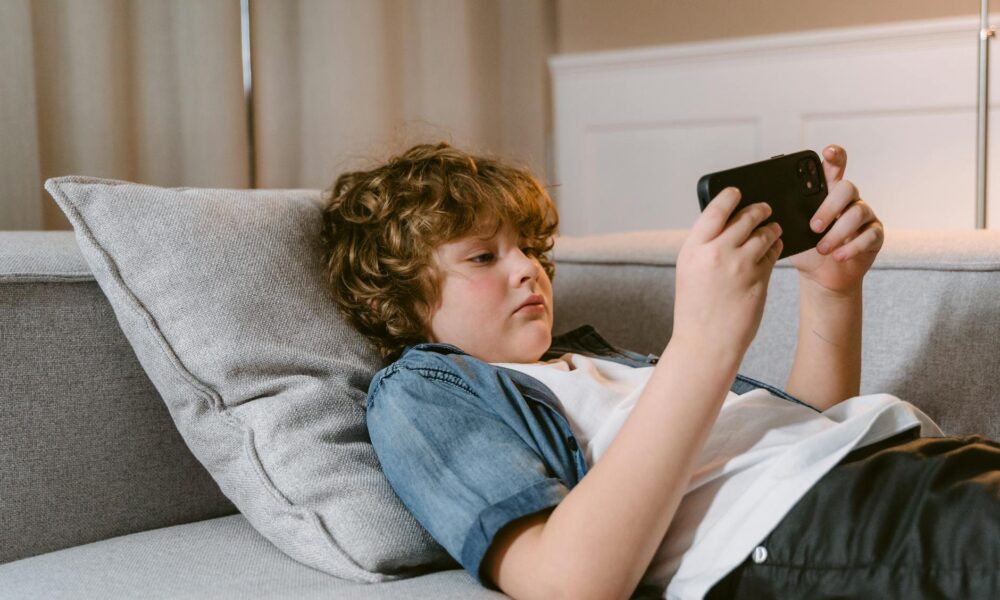 a boy using a smartphone while lying on a sofa